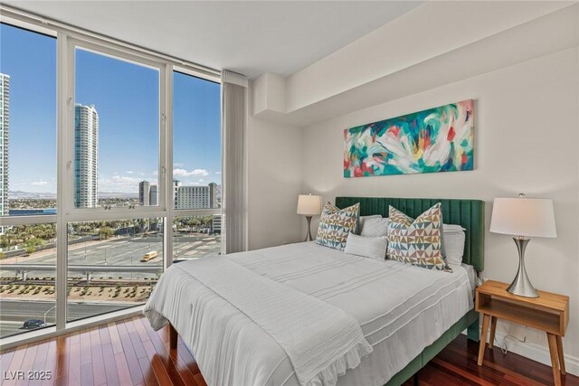 bedroom with floor to ceiling windows, wood finished floors, and a city view