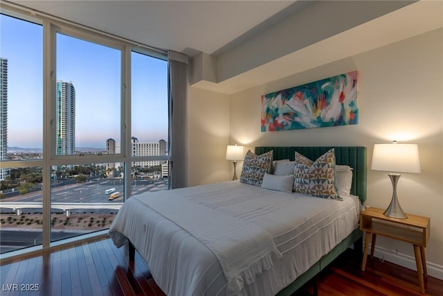 bedroom featuring dark wood-style floors, a view of city, and baseboards