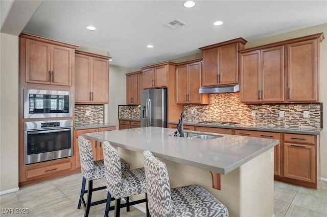 kitchen featuring stainless steel appliances, under cabinet range hood, a breakfast bar area, an island with sink, and recessed lighting