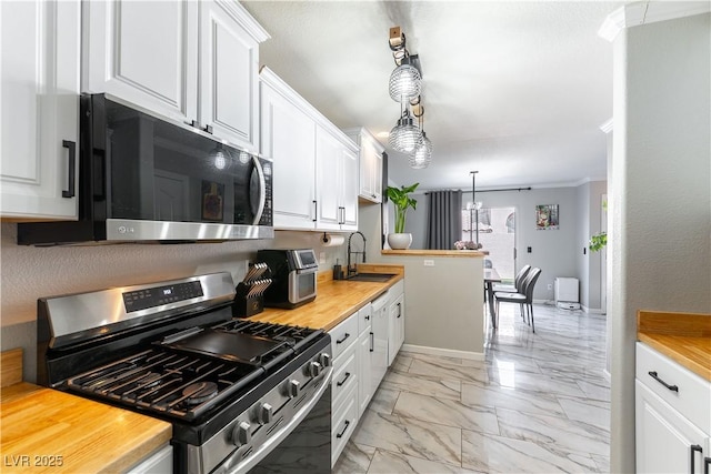 kitchen with stainless steel range with gas stovetop, a sink, white cabinetry, light marble finish flooring, and ornamental molding