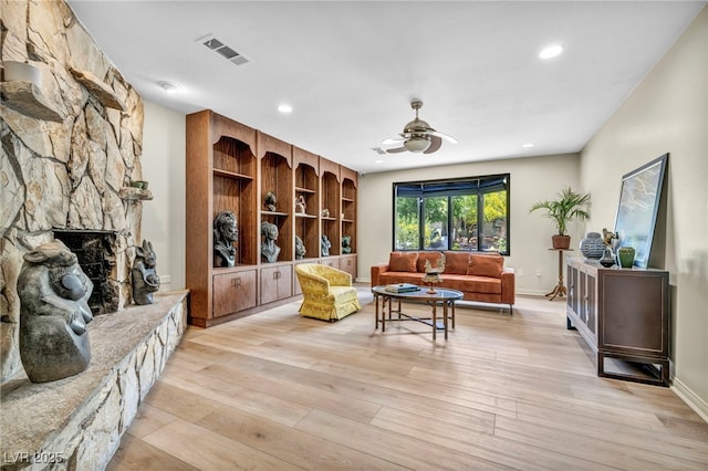 living room featuring ceiling fan, light wood-type flooring, a fireplace, recessed lighting, and baseboards