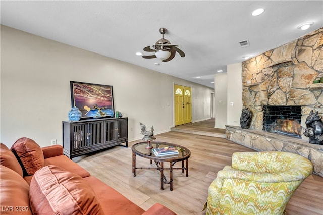 living room with ceiling fan, wood finished floors, baseboards, a stone fireplace, and recessed lighting