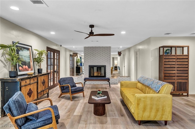 living area featuring light wood finished floors, a ceiling fan, recessed lighting, french doors, and a brick fireplace