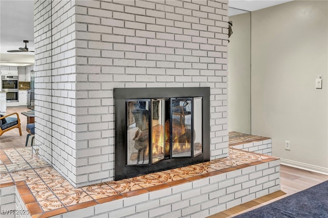 detailed view of a brick fireplace, double oven, wood finished floors, and baseboards