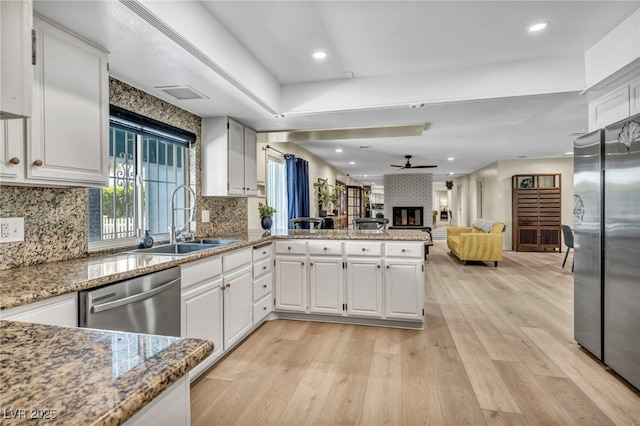 kitchen featuring a sink, stainless steel appliances, a brick fireplace, light wood finished floors, and recessed lighting