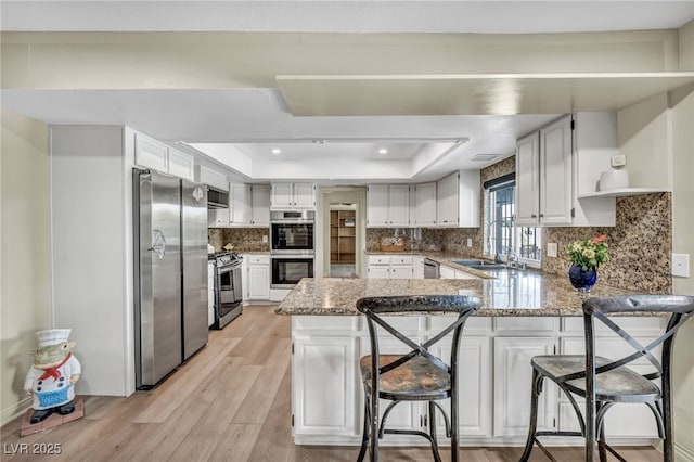 kitchen with stainless steel appliances, a tray ceiling, a peninsula, a sink, and open shelves