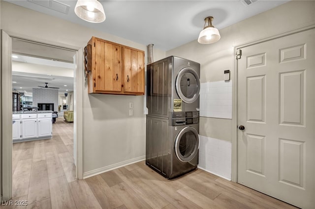 laundry room featuring stacked washer and clothes dryer, cabinet space, light wood finished floors, a ceiling fan, and baseboards