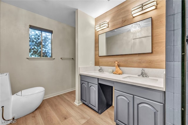 bathroom with wood finished floors, baseboards, double vanity, and toilet