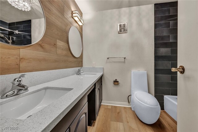 bathroom with wood finished floors, baseboards, toilet, double vanity, and a shower