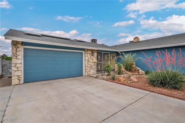 ranch-style home featuring stone siding, driveway, an attached garage, roof mounted solar panels, and cooling unit