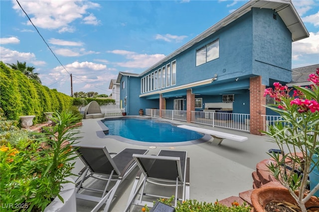 outdoor pool featuring fence, a patio, and a diving board