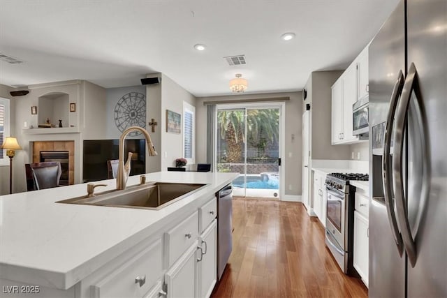 10046 Floragold Ct, Las Vegas, NV 89147 - kitchen with stainless steel appliances, a sink, a tile fireplace, white cabinets, and wood finished floors