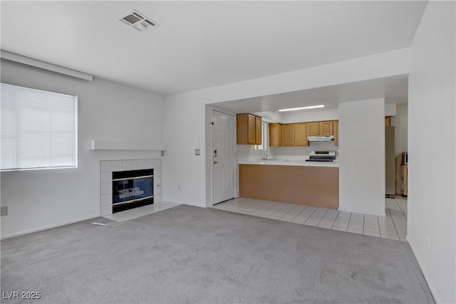 unfurnished living room with light carpet, a sink, a tile fireplace, and light tile patterned floors