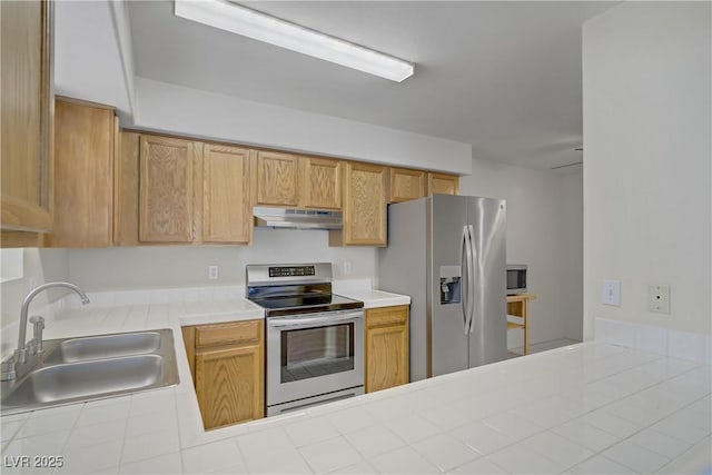 kitchen featuring stainless steel appliances, a sink, under cabinet range hood, tile counters, and a peninsula