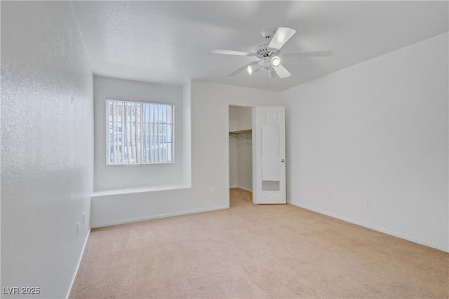 unfurnished bedroom with carpet, a spacious closet, a ceiling fan, baseboards, and a closet