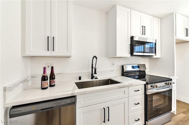 kitchen with appliances with stainless steel finishes, a sink, light stone counters, and white cabinetry