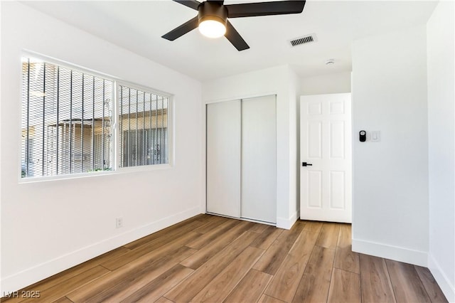 unfurnished bedroom featuring multiple windows, baseboards, a closet, and wood finished floors