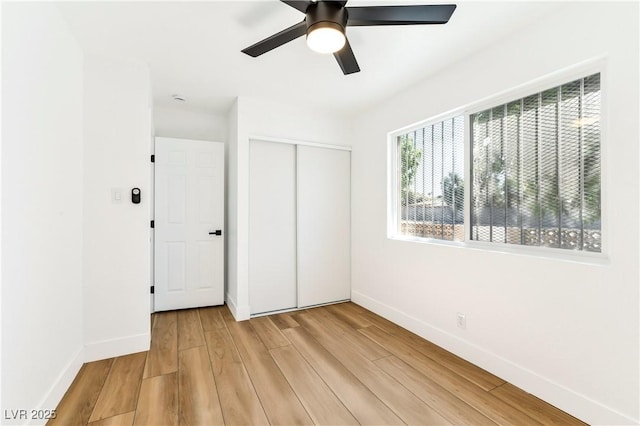 unfurnished bedroom featuring baseboards, light wood-style floors, a closet, and a ceiling fan