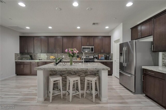 205 Piedmont Alps St, Henderson, NV 89012 - kitchen with stainless steel appliances, an island with sink, decorative backsplash, dark brown cabinets, and recessed lighting