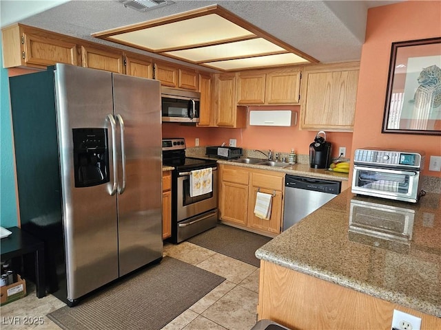 kitchen with stainless steel appliances, a sink, light tile patterned floors, and light stone counters