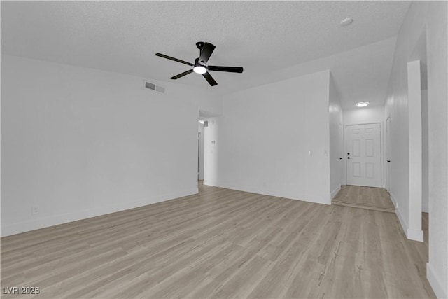 spare room featuring light wood-type flooring, a ceiling fan, a textured ceiling, and baseboards