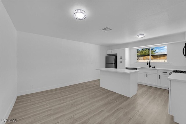 kitchen featuring stainless steel appliances, a sink, light wood-type flooring, a kitchen island, and light countertops