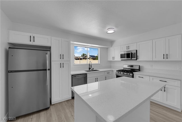 kitchen with appliances with stainless steel finishes, a sink, light wood-style floors, white cabinets, and a textured ceiling