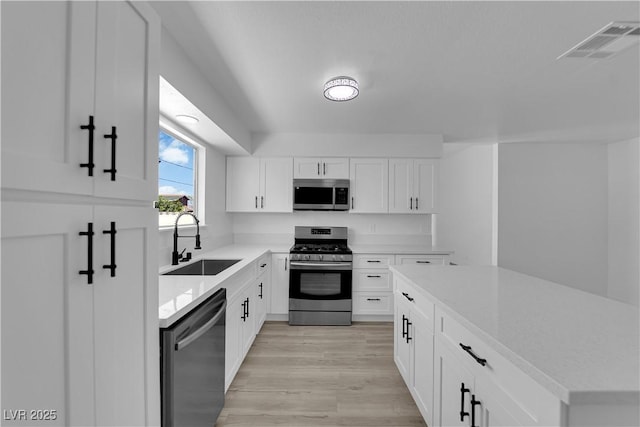 kitchen with stainless steel appliances, a sink, light wood-type flooring, light countertops, and white cabinetry