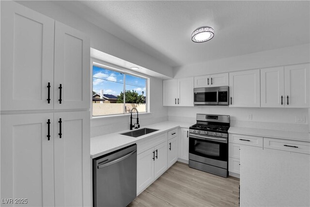 kitchen with appliances with stainless steel finishes, a sink, light countertops, and white cabinets