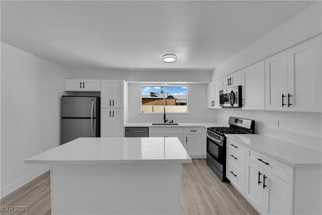 kitchen featuring appliances with stainless steel finishes, a kitchen island, a sink, light countertops, and light wood-type flooring