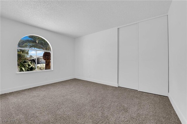 unfurnished bedroom with carpet flooring, a textured ceiling, a closet, and baseboards