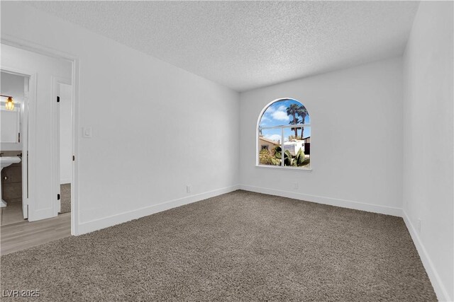 spare room featuring carpet flooring, a textured ceiling, and baseboards
