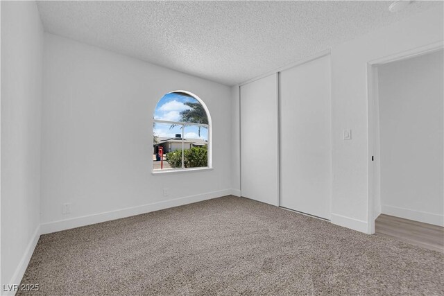 unfurnished bedroom featuring a textured ceiling, carpet floors, a closet, and baseboards