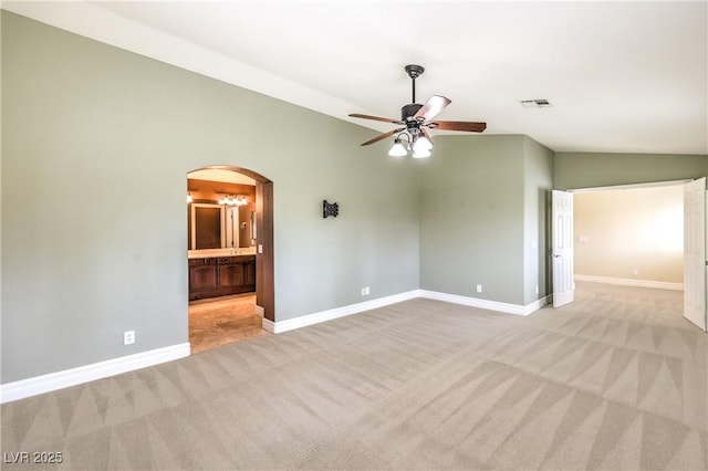 empty room with vaulted ceiling, carpet floors, a ceiling fan, baseboards, and arched walkways