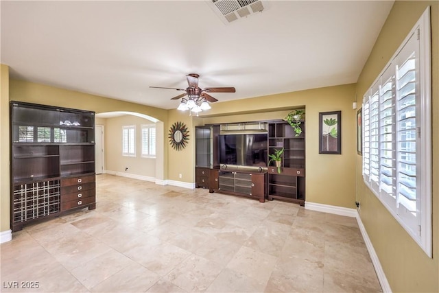 unfurnished living room featuring ceiling fan, baseboards, arched walkways, and tile patterned floors
