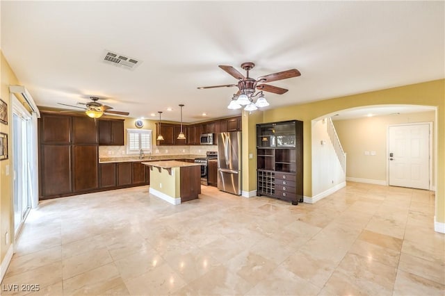 kitchen featuring stainless steel appliances, ceiling fan, arched walkways, a kitchen island, and tasteful backsplash