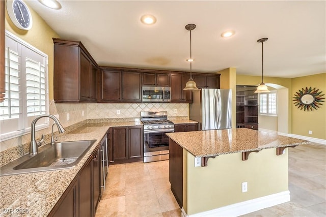 kitchen featuring stainless steel appliances, a sink, a kitchen island, backsplash, and dark brown cabinetry
