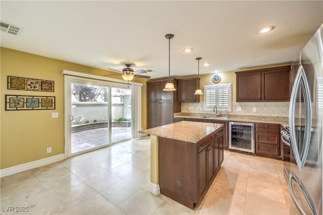 kitchen with wine cooler, freestanding refrigerator, a sink, tasteful backsplash, and light stone countertops