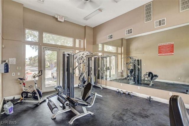 gym with a towering ceiling, baseboards, healthy amount of natural light, and a ceiling fan
