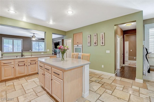 6409 Sea Swallow St, North Las Vegas, NV 89084 - kitchen with light brown cabinetry, white oven, light countertops, ceiling fan, and stone tile floors