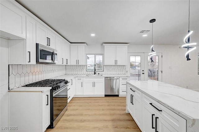 kitchen with appliances with stainless steel finishes, backsplash, white cabinetry, hanging light fixtures, and recessed lighting