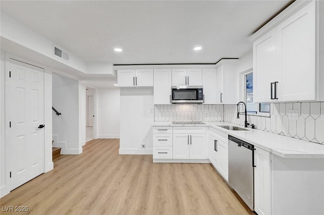 kitchen with stainless steel appliances, a sink, light wood finished floors, white cabinetry, and recessed lighting