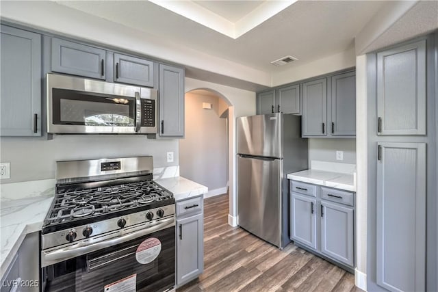 541 Indian Bluff St Unit 201, Las Vegas, NV 89145 - kitchen featuring stainless steel appliances, arched walkways, gray cabinets, wood finished floors, and light stone countertops