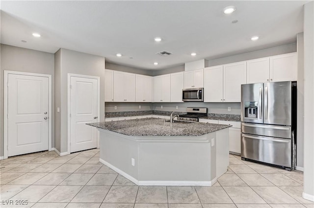 kitchen featuring stainless steel appliances, a sink, dark stone counters, white cabinetry, and light tile patterned flooring