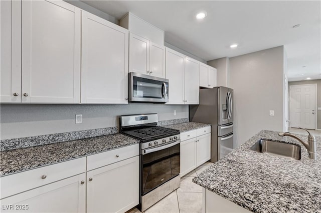 kitchen featuring stainless steel appliances, a sink, white cabinetry, dark stone countertops, and recessed lighting