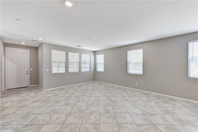 empty room with healthy amount of natural light, light tile patterned floors, recessed lighting, and baseboards