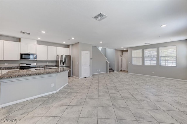 kitchen with stainless steel appliances, recessed lighting, dark stone countertops, open floor plan, and white cabinetry