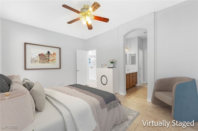 bedroom with light tile patterned floors, arched walkways, ensuite bath, ceiling fan, and baseboards
