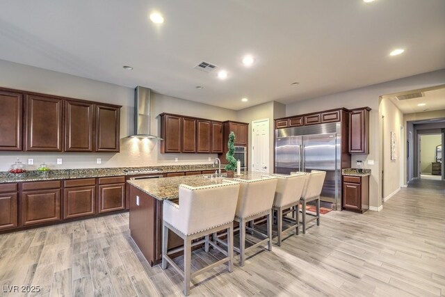 9760 Arch Canyon Ct, Las Vegas, NV 89149 - kitchen with stainless steel appliances, wall chimney exhaust hood, a kitchen bar, light wood finished floors, and recessed lighting
