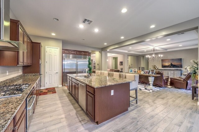 9760 Arch Canyon Ct, Las Vegas, NV 89149 - kitchen featuring open floor plan, a kitchen breakfast bar, wall chimney exhaust hood, appliances with stainless steel finishes, and light wood-type flooring